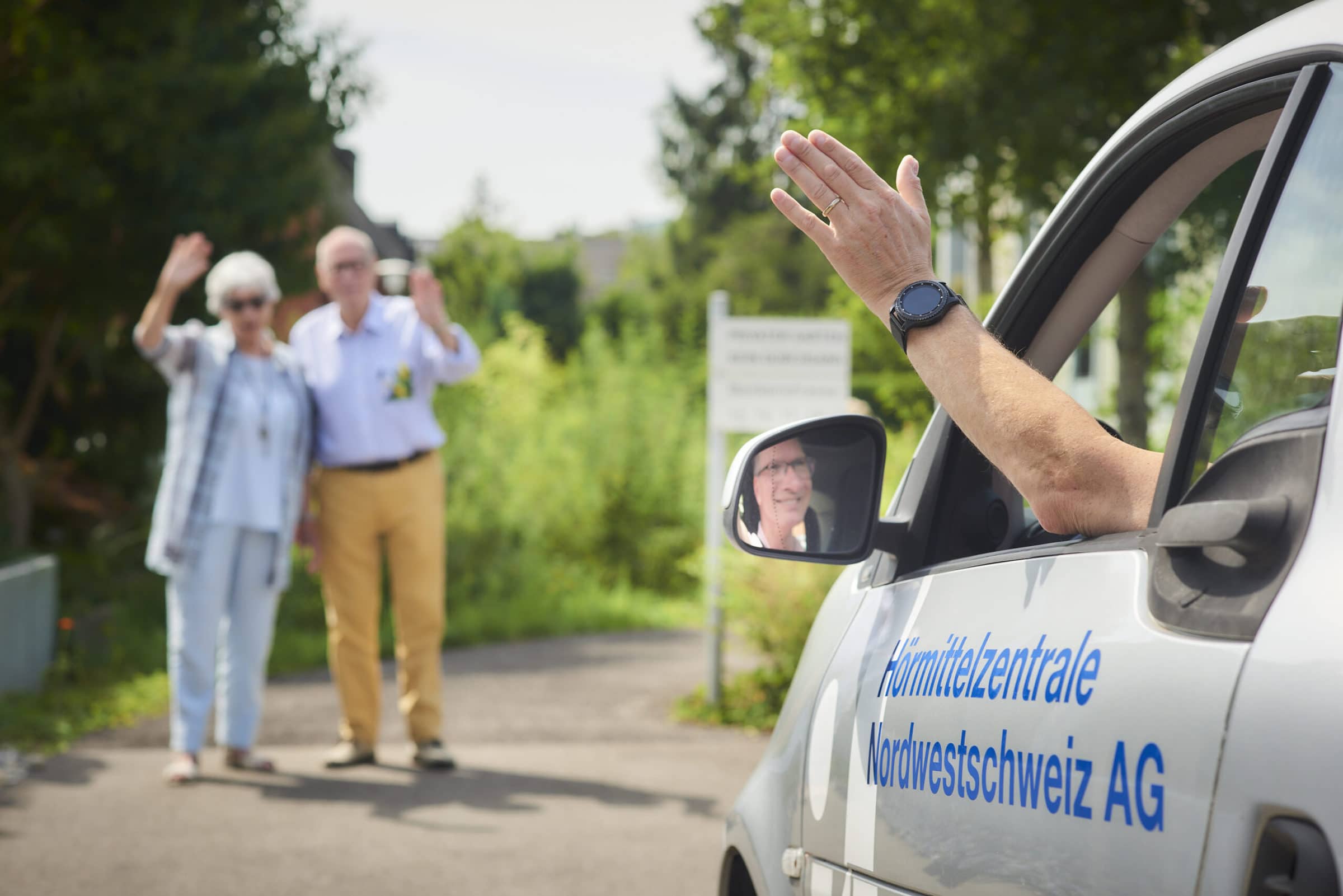 Akustiker winkt nach dem Hausbesuch aus dem Auto den Kunden zu